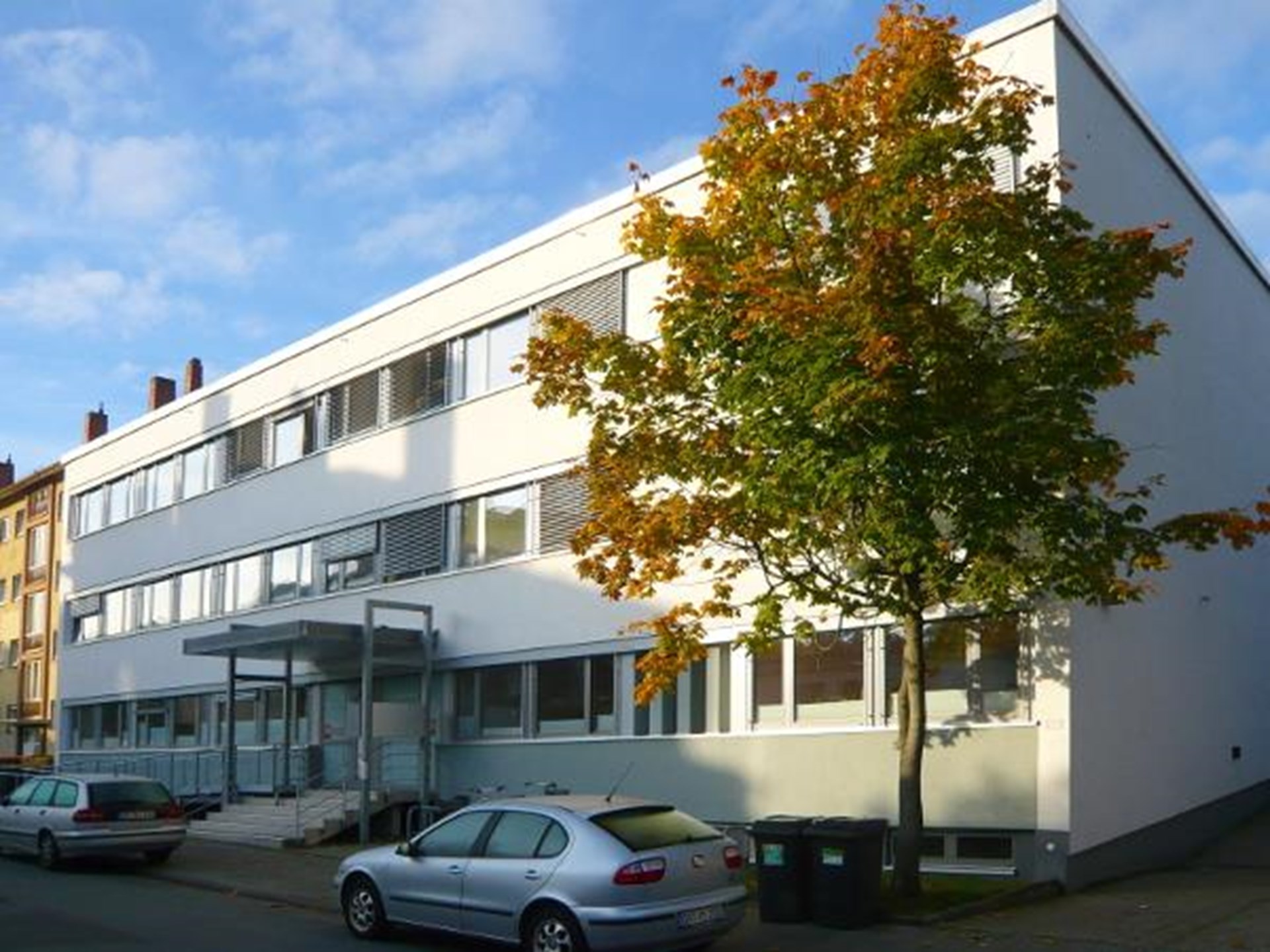 Gebäude mit Eingangstür, davor Treppe und Rollstuhlrampe